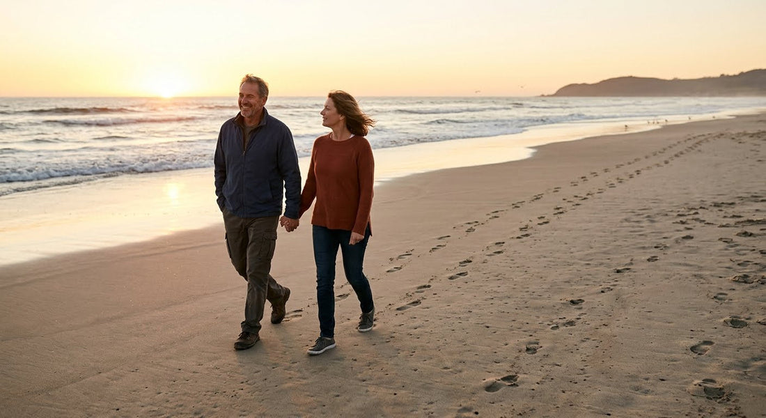 A couple walking together along a quiet beach at golden hour with footprints behind them in the sand